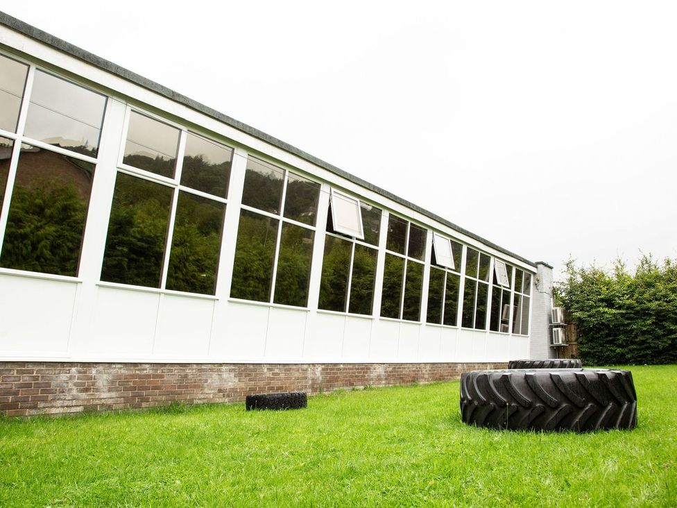 An outdoor view of a building with windows and a tire on the grass at Fir Tree Lodge, Coniston 3, White Cross Bay near Windermere