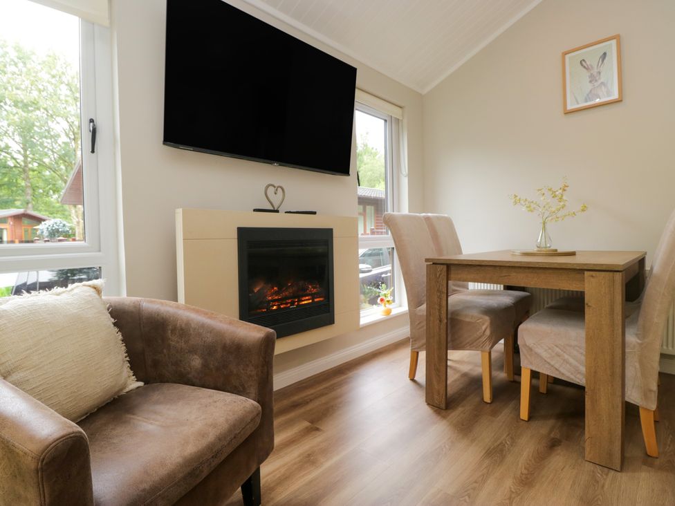 A living room with an armchair, table, and fireplace at Fir Tree Lodge, White Cross bay on Windermere, Troutbeck Bridge
