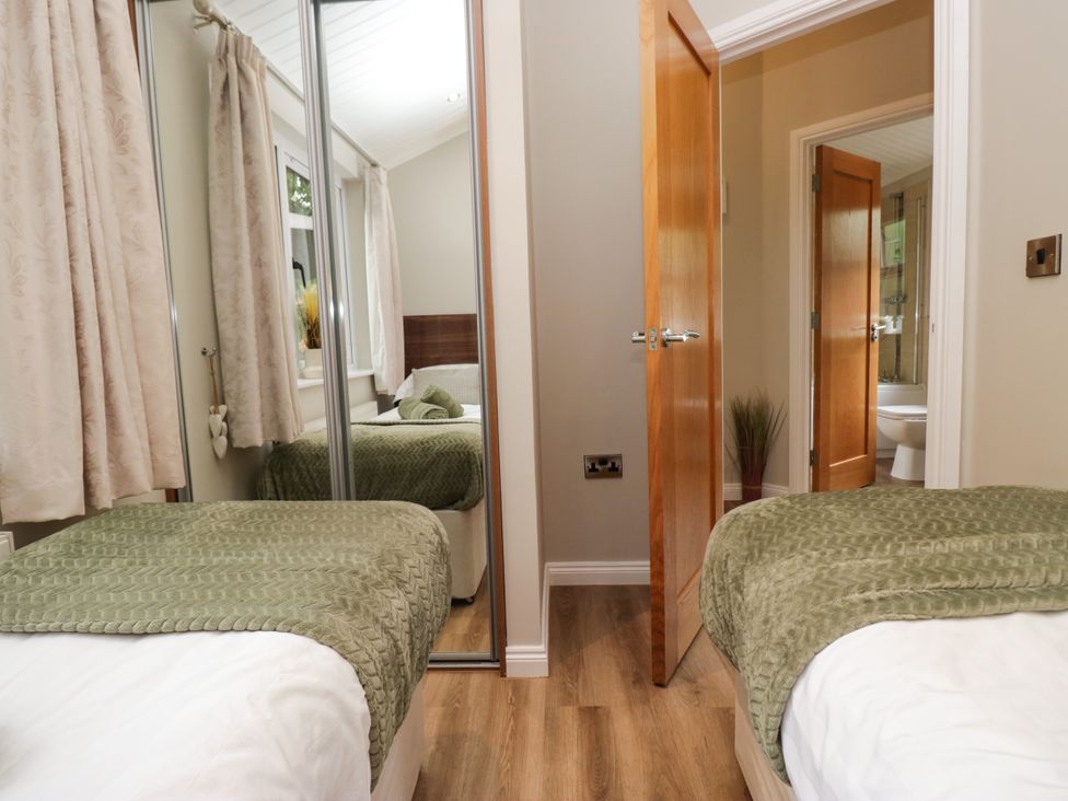 A bedroom with two beds and a door leading to a bathroom at Fir Tree Lodge in White Cross bay on Windermere, Troutbeck Bridge