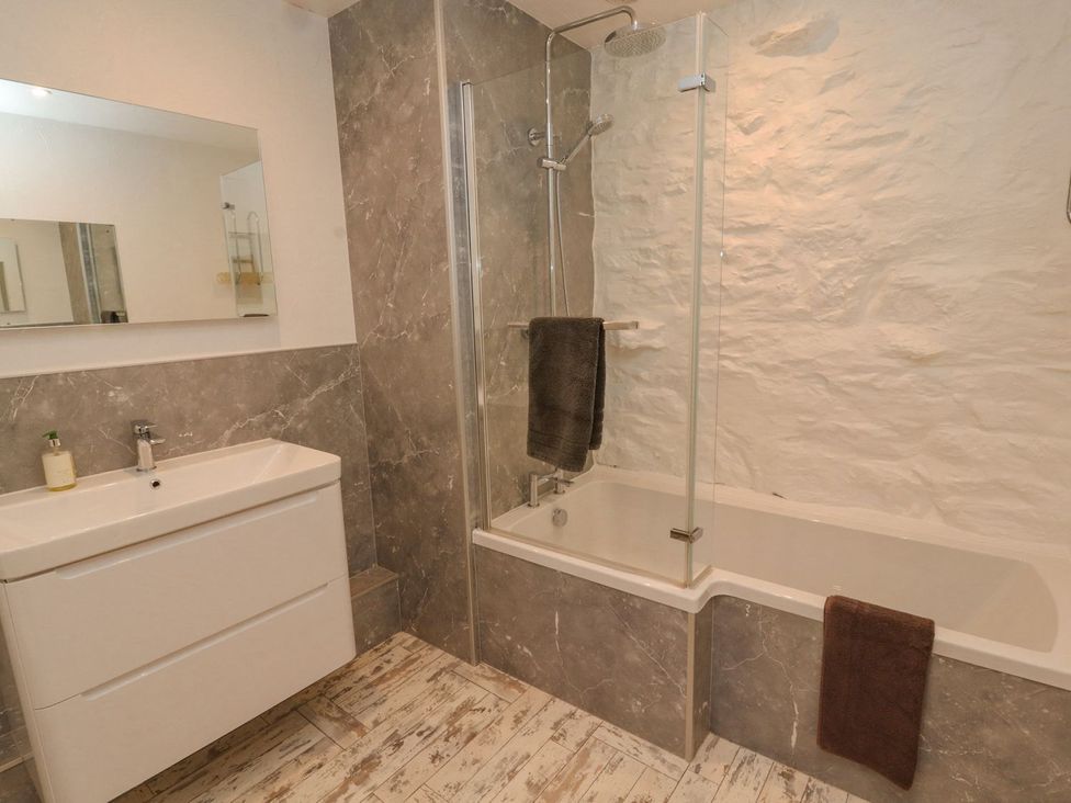 A bathroom with a sink, mirror, shower, and bathtub at Mellfell Cottage near Watermillock