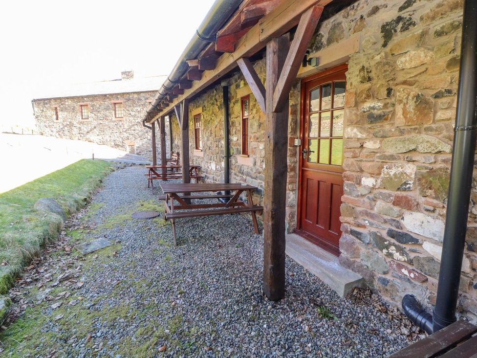An outdoor area with a stone wall and wooden tables at Mellfell Cottage near Watermillock