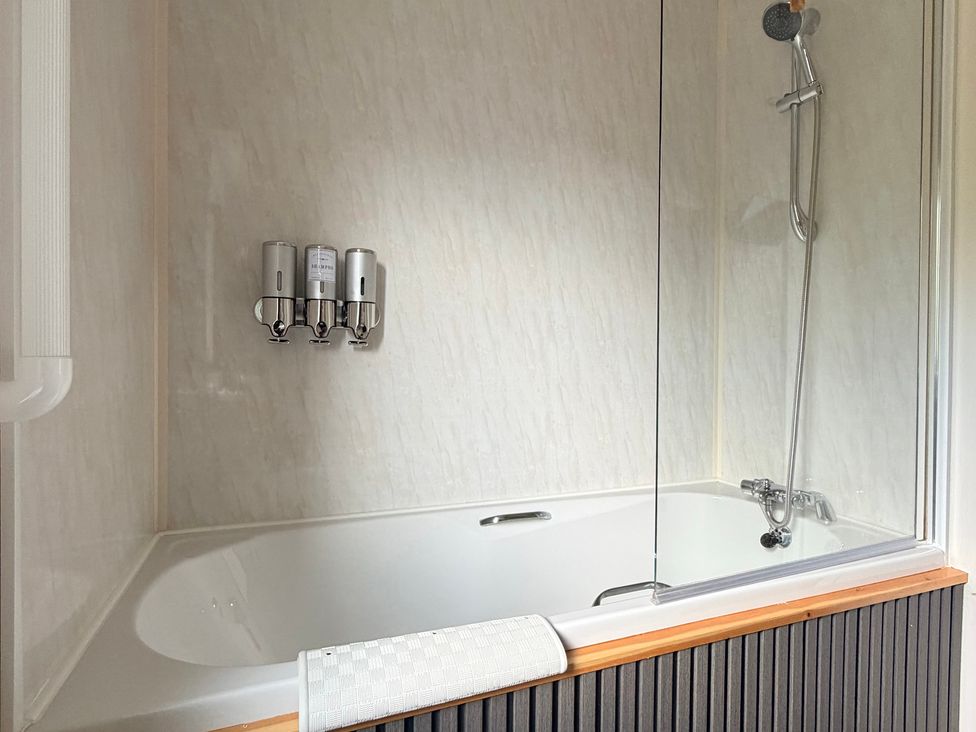 A bathtub with showerhead and soap dispensers at Boutique Lodge in Cheriton Bishop