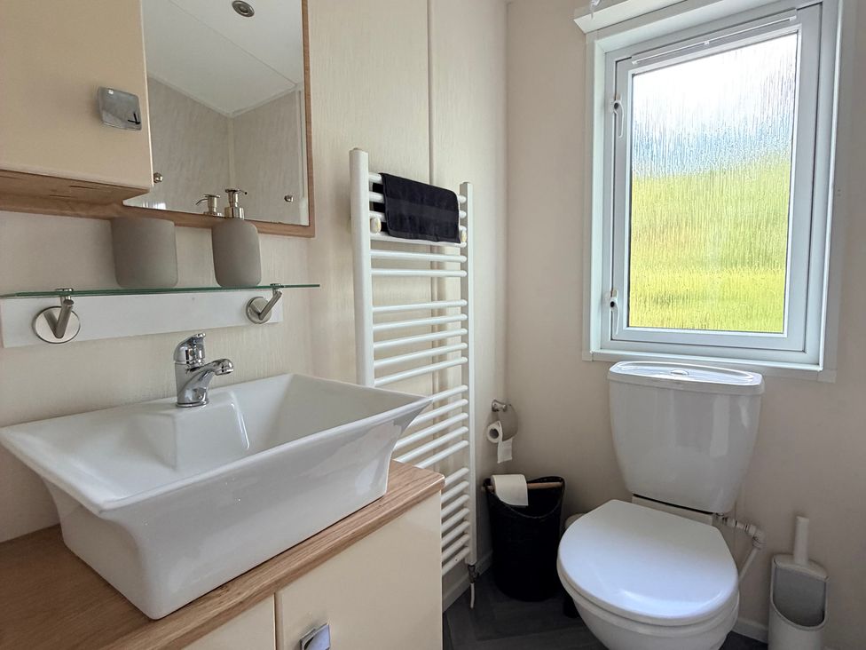 A bathroom with a sink, toilet, mirror, and towel rail at Boutique Lodge in Cheriton Bishop