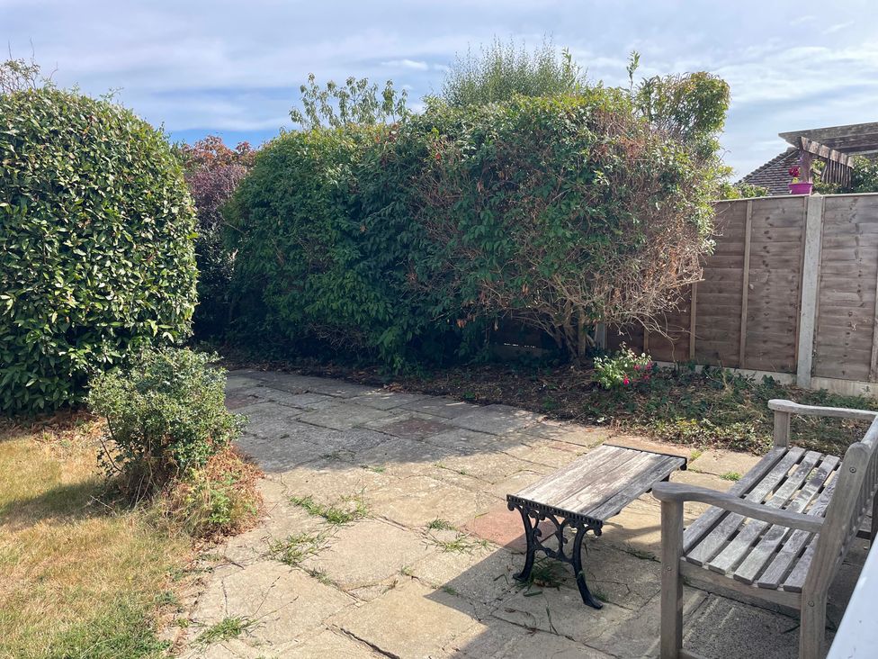 A garden with a patio and a wooden chair at Summer Cottage in Rustington
