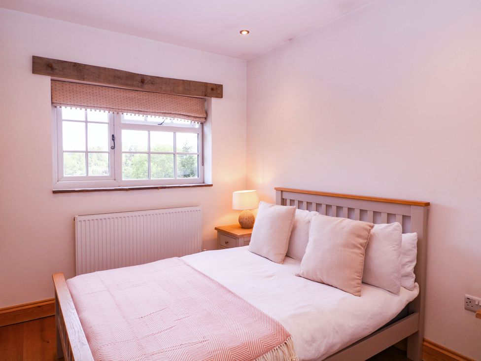 A bedroom with a bed, pillows, lamp, and window at The burrow at Aveling Cottage in Lydney