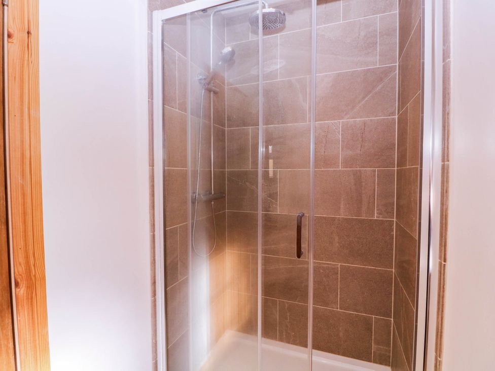 A shower enclosure with tiles and a showerhead at The burrow at Aveling Cottage in Lydney