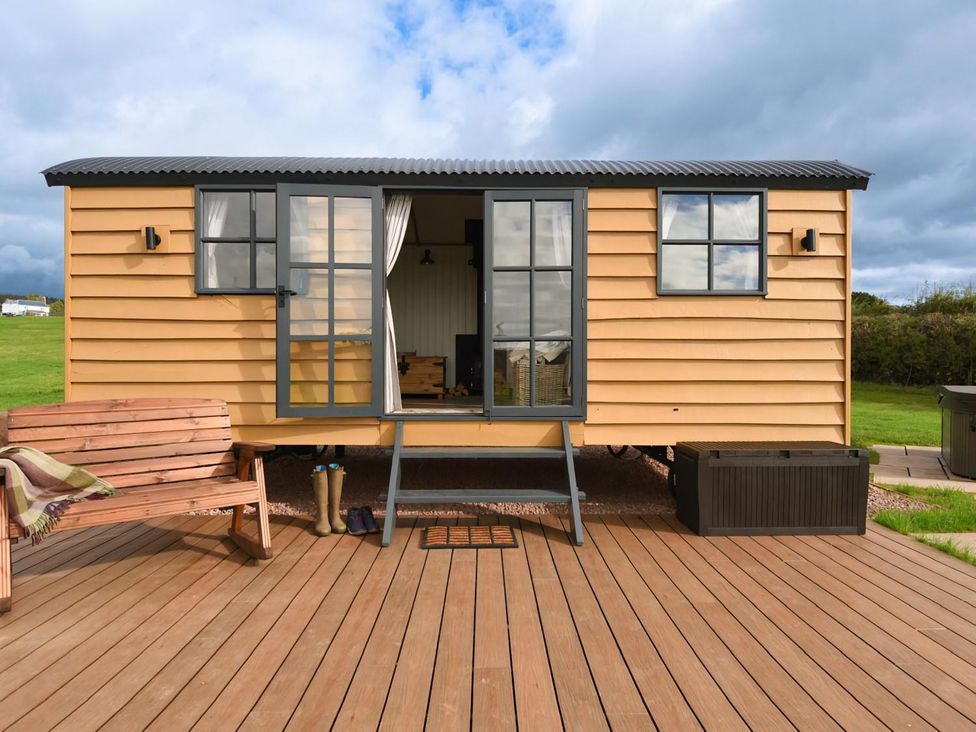 A shepherd hut with a wooden deck and bench at Shepherd Hut at Garden Cottage near Woolaston