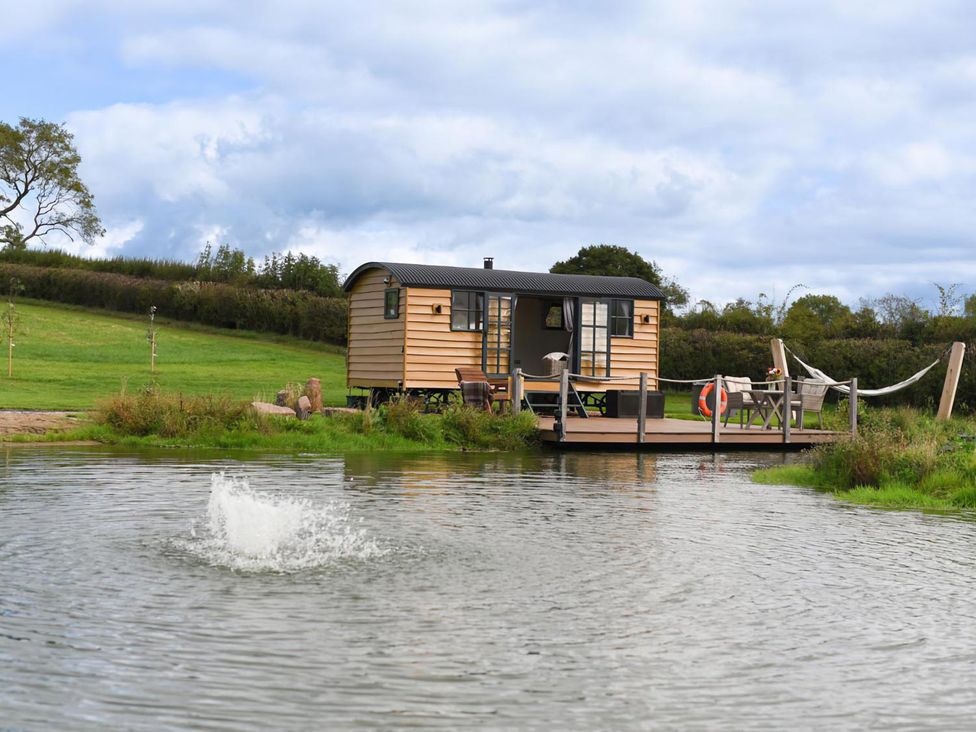 A hut with a deck by a pond at Shepherd Hut at Garden Cottage near Woolaston
