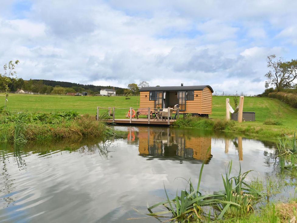 A shepherd hut on a deck by a pond at Shepherd Hut at Garden Cottage near Woolaston