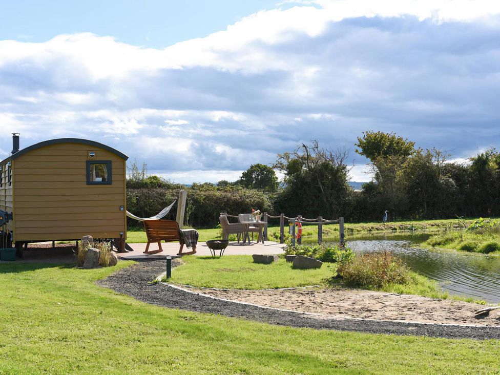 A shepherd hut by a pond with seating area at Shepherd Hut at Garden Cottage near Woolaston