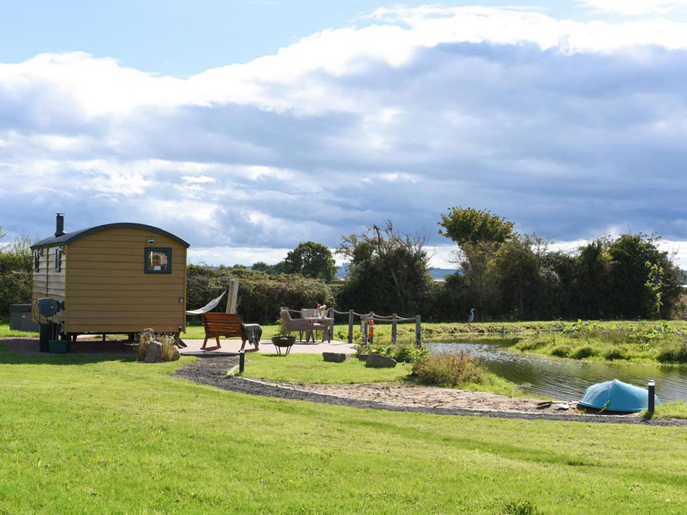 A shepherd hut with outdoor seating and a pond at Shepherd Hut at Garden Cottage near Woolaston