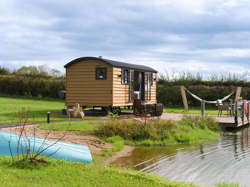 A shepherd hut near water with a dock and hammock at Shepherd Hut at Garden Cottage near Woolaston