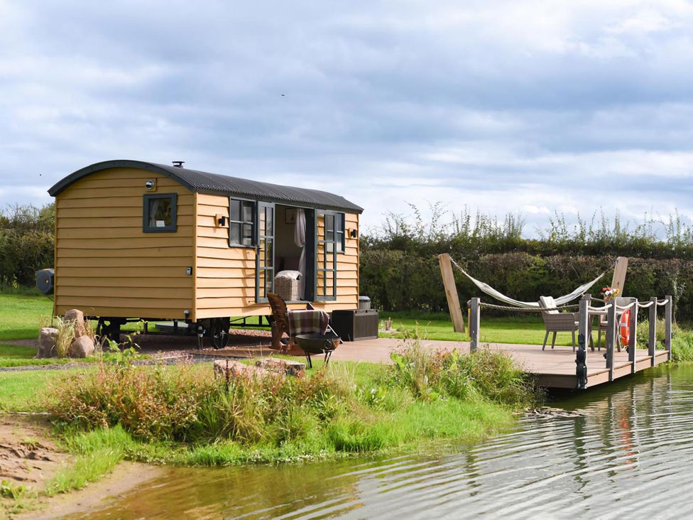 A shepherd hut with a decking area and hammock at Shepherd Hut at Garden Cottage near Woolaston