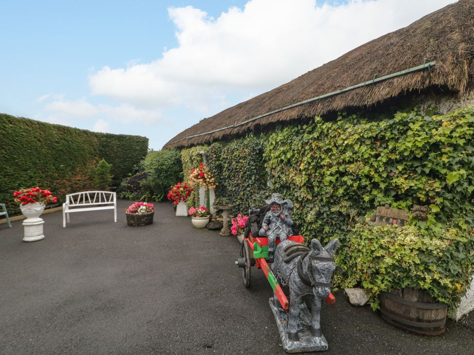 An outdoor area with ivy, flowers, a statue on a stone cart, and a barrel at Teresa's Cottage