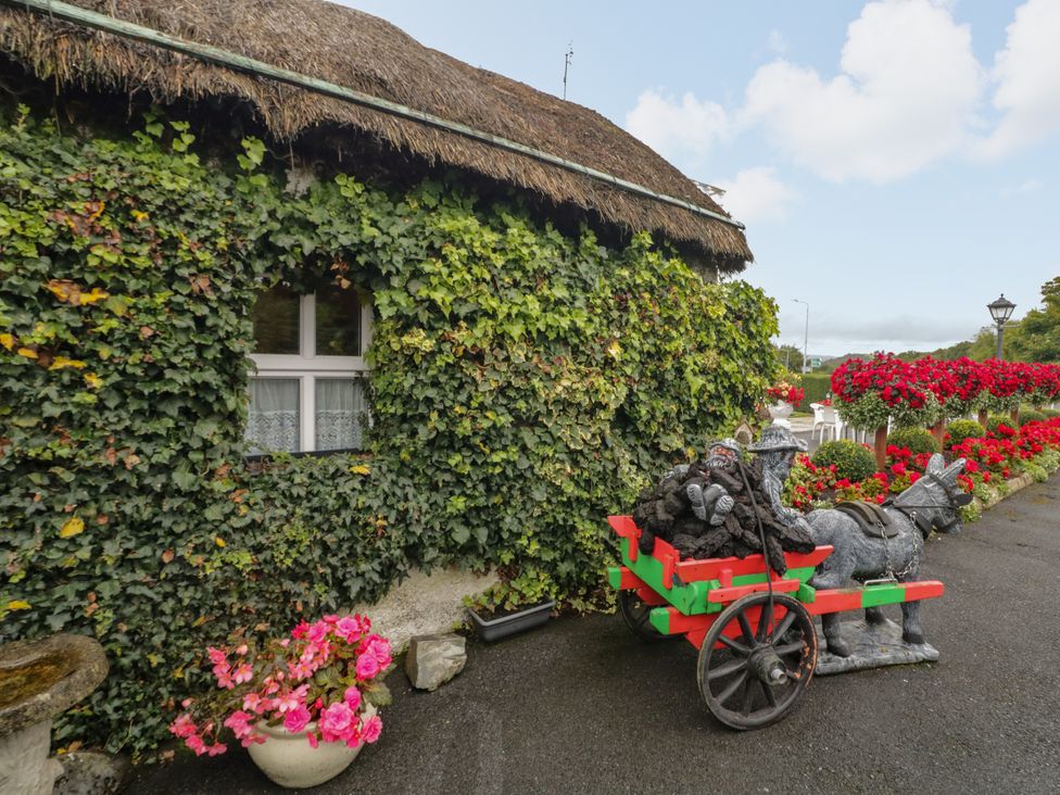 A thatched cottage with ivy and decorative cart at Teresa's Cottage