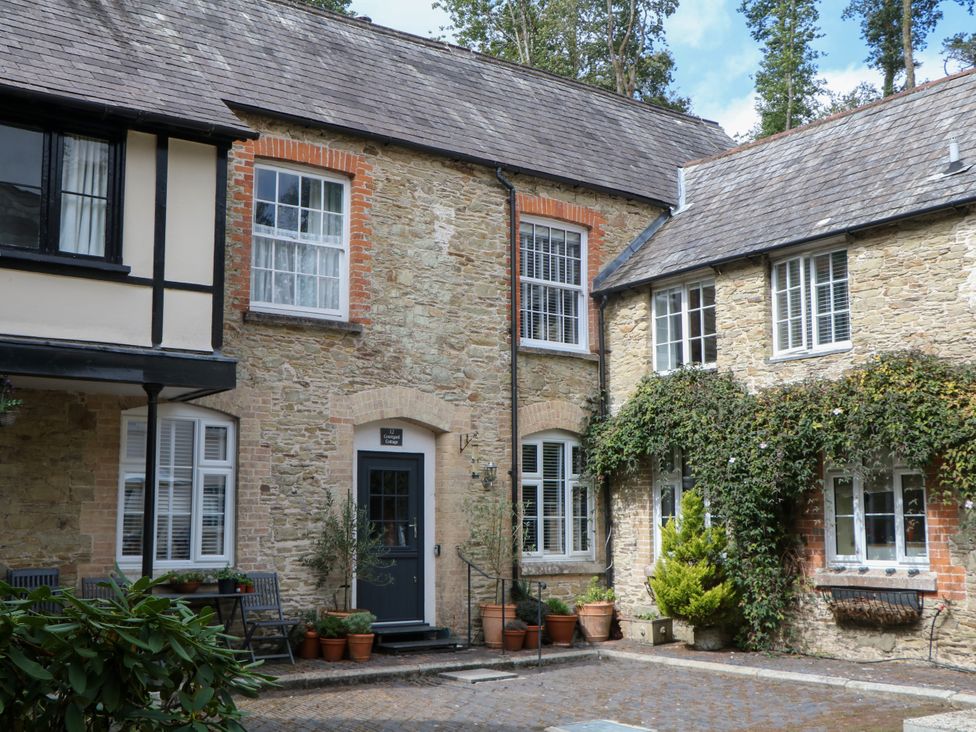 A stone building with windows and door framed by potted plants at 12 Courtyard Cottage at Sheplegh Court Totnes