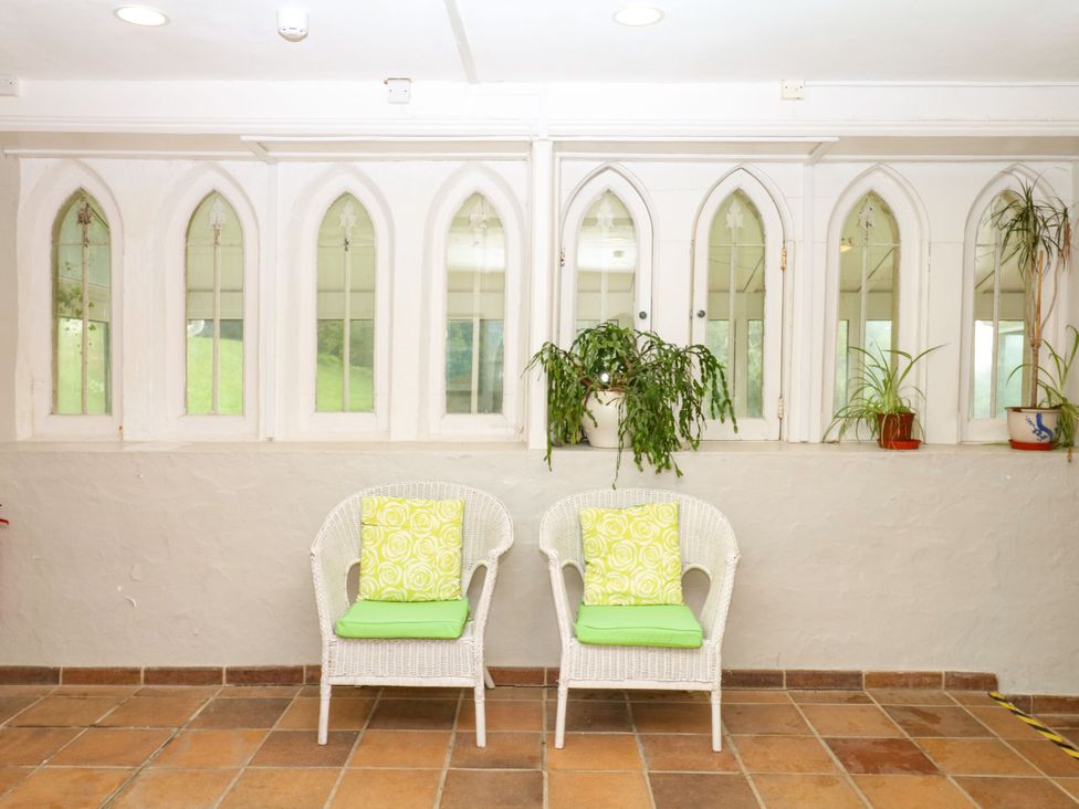 A conservatory with armchairs and plants at 12 Courtyard Cottage at Sheplegh Court, Totnes