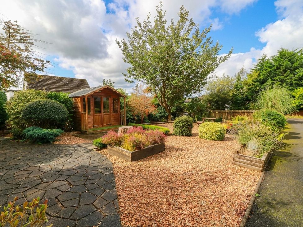 A garden with a wooden shed and flower beds at Camusfearna in Dalbeattie