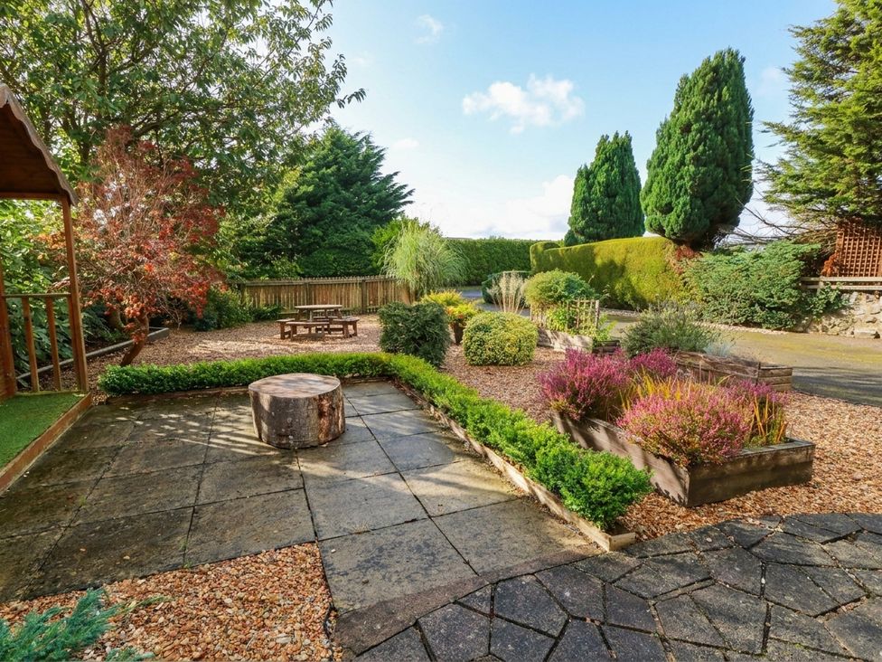 A garden with a wooden table and seating area at Camusfearna in Dalbeattie