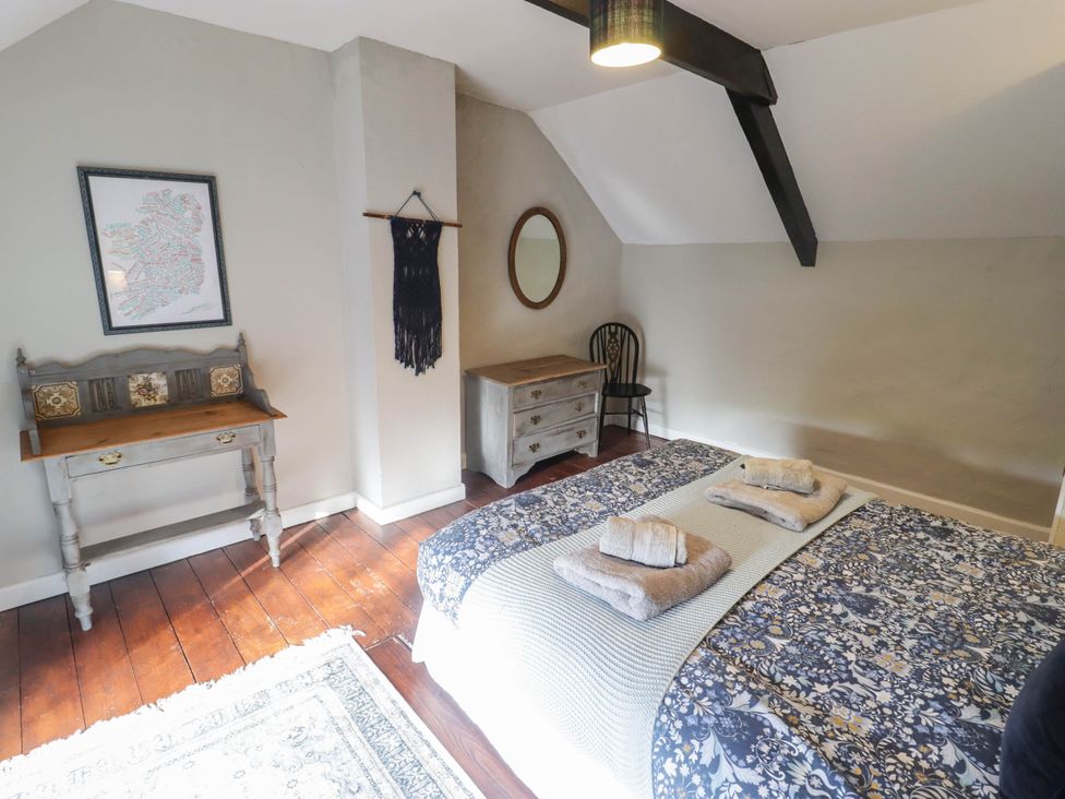 A bedroom with a bed, table, chair, and mirror at Ty'r Wennol in Fishguard