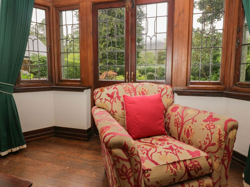 A sitting room with a floral armchair and large windows at White Gables in Grasmere