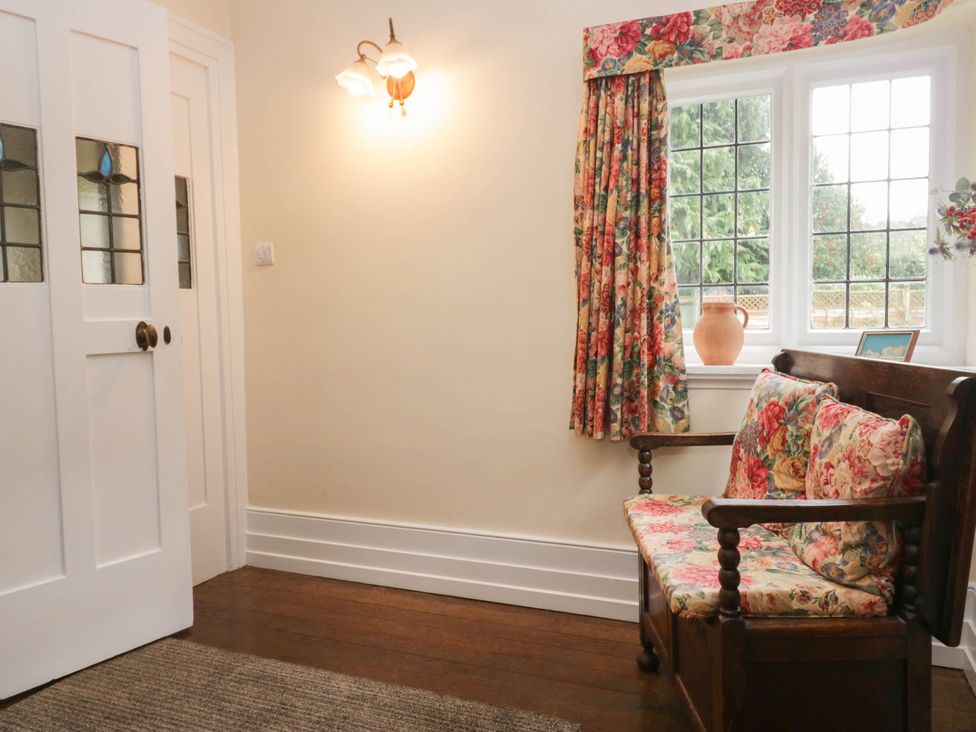 An entryway with a wooden settee and floral curtains at White Gables in Grasmere