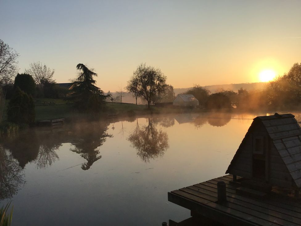 A tranquil lake at sunrise with trees and a fishing hut at Chestnut Lodge Worcester
