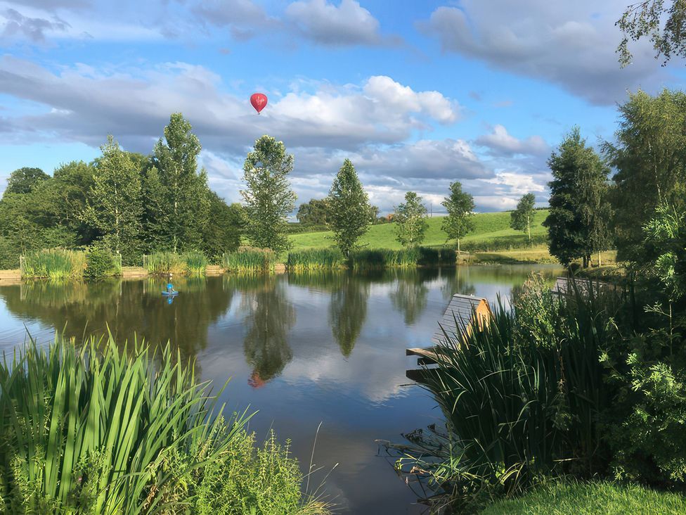 A pond with trees and a hot air balloon at Kingfisher in Worcester