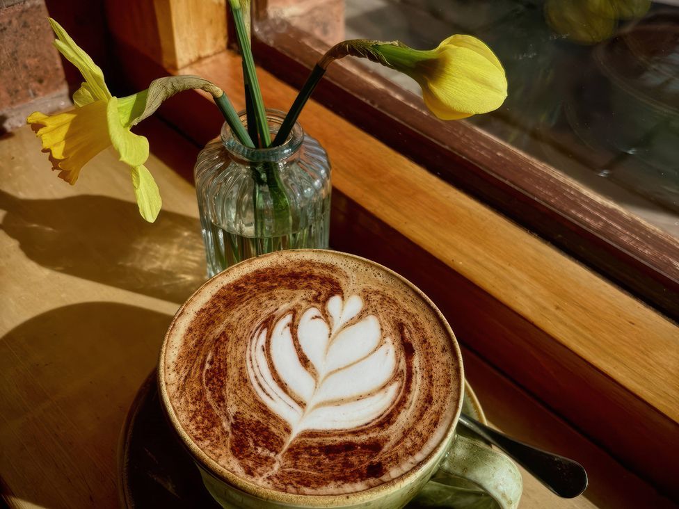 A cup of coffee with a leaf design and a vase with flowers at Chaff House in Worcester