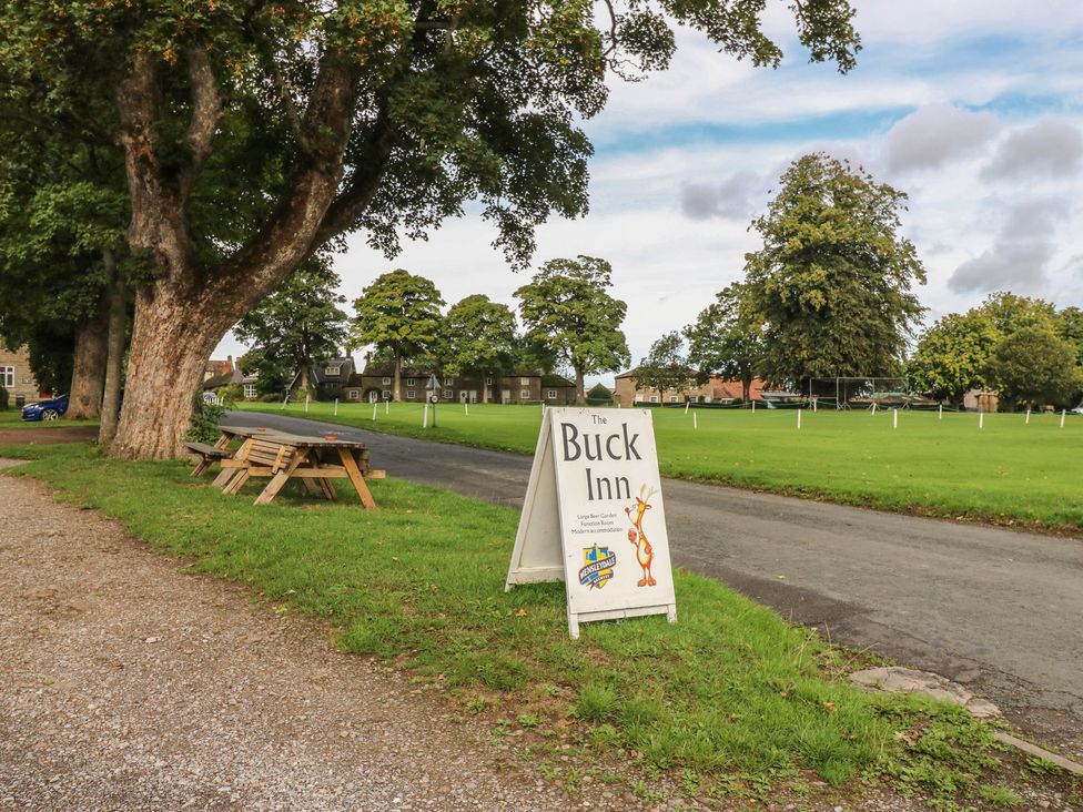 A sign for The Buck Inn next to a pathway with trees and benches in Ripon