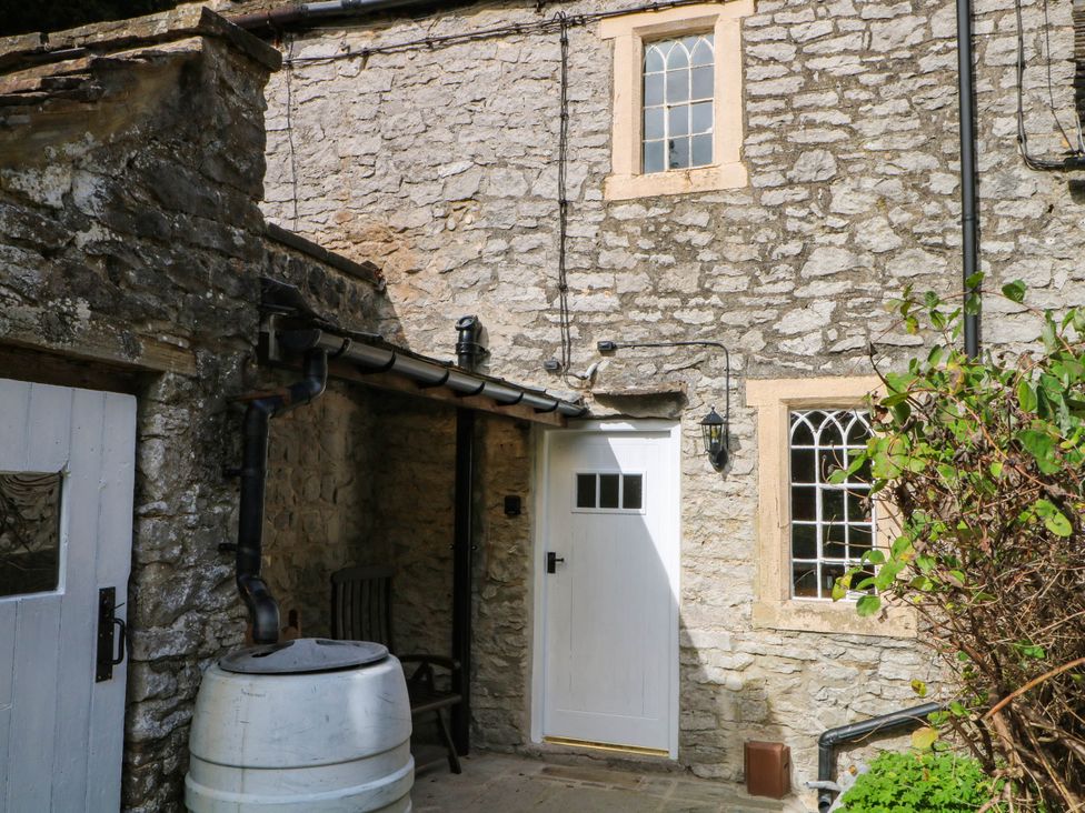 An outdoor view of a stone cottage with a white door and a bush at 73 Ravensdale Cottages Cressbrook near Litton Derbyshire
