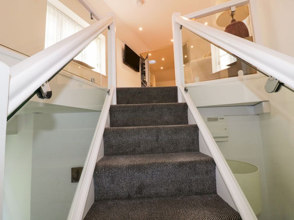 Stairs with a glass railing and tv at Fishermans Loft Mevagissey