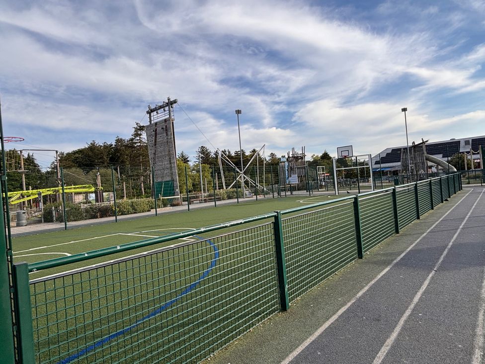An outdoor sports area with a fence, basketball hoop, climbing wall and artificial turf