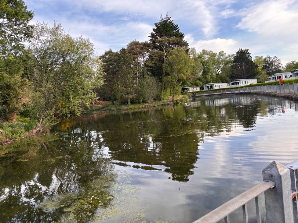 A pond surrounded by trees with static caravans in the background at an outdoor location