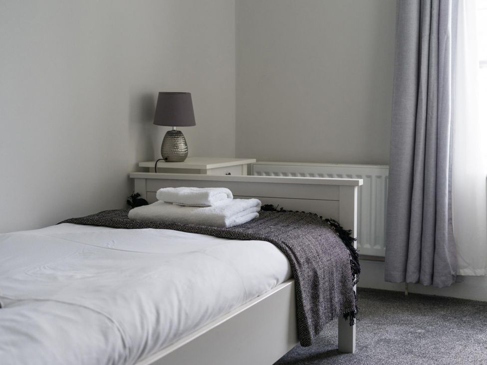 A bedroom with a bed, lamp, and towels at East House-Sleeps 5-Pet friendly-Garden-Parking in Stakeford
