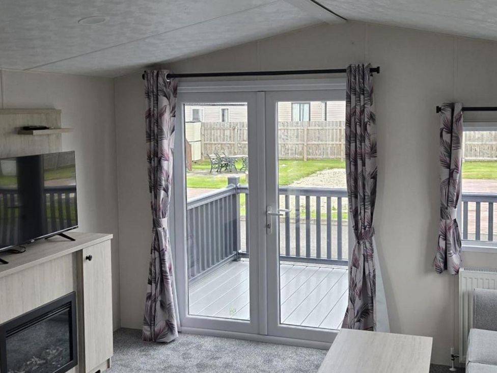 A living room with a television and door leading to a deck at 3 Bedroom Cabin Sleeps 6 - Shared Pool & Shared Hot Tub, Flamingo Land Resort near Malton