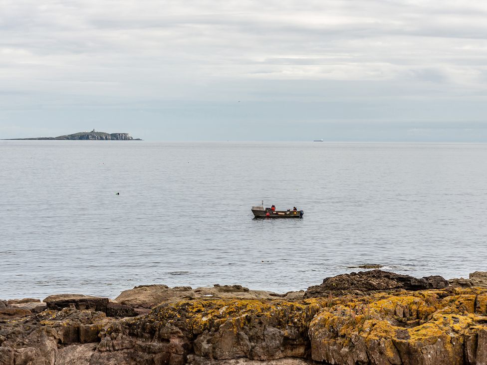 A boat on water with rocky shore and island in the distance at Cellardyke 3-Bed House, Sleeps 6 with Sea Terrace, Cellardyke