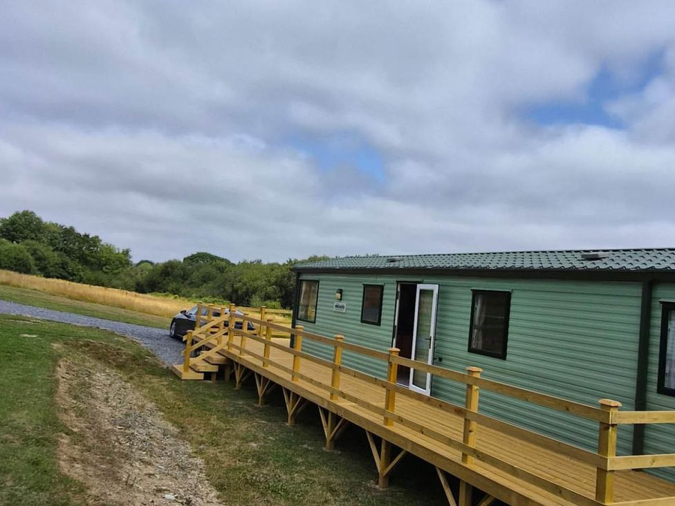 A mobile home with a wooden deck and a car parked at Cabin - Sleeps 6 - Outdoor Pool and Parking in Cenarth