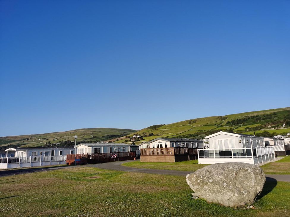 Mobile homes and a rock on grass with mountains in the background at Snowdonia Sunbeach Holiday Sea and Mountain view Llwyngwril