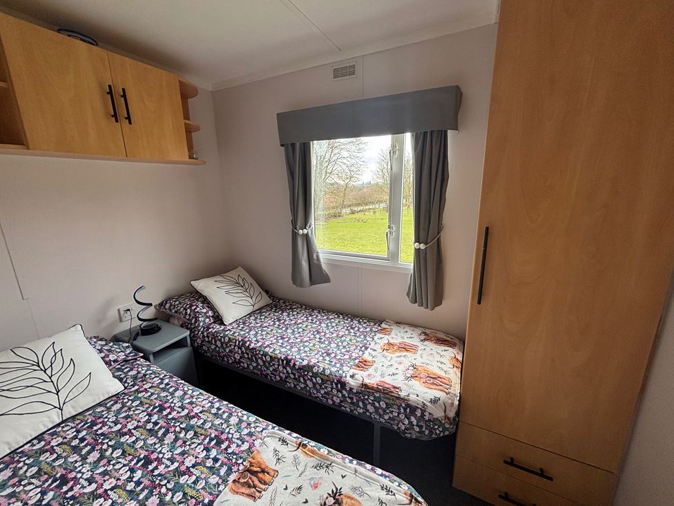 A bedroom with two beds and a window at No 38 Heilan Hoose at Three Lochs Holiday Park near Newton Stewart