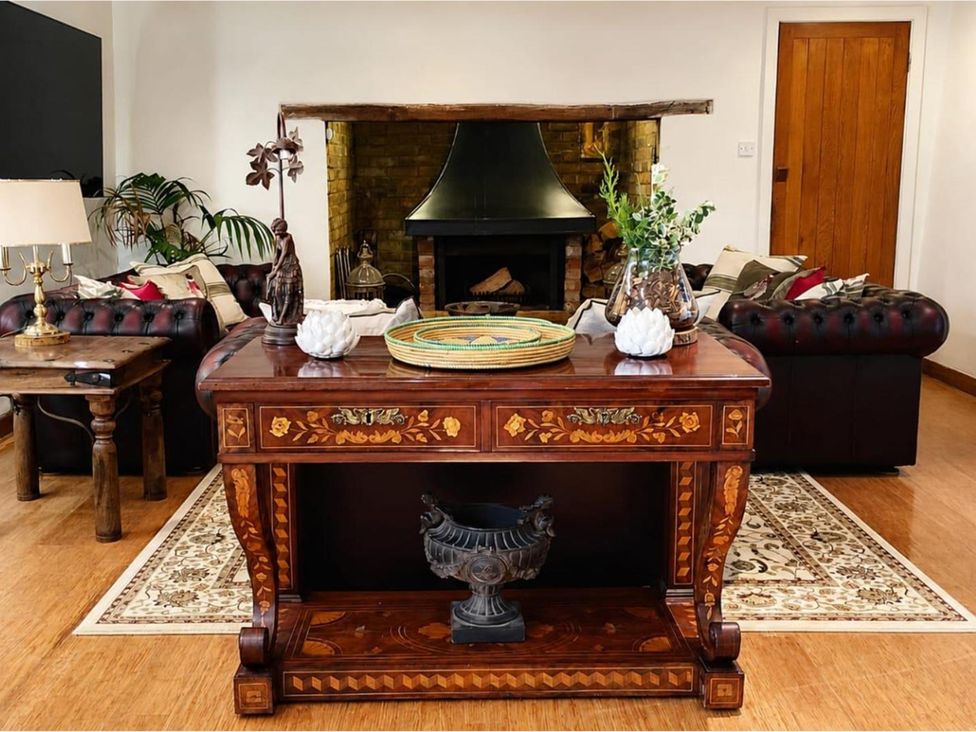 A living room with a wooden table, sofa, and fireplace at Sharvels Oast House - Pool, Tennis, Luxury Home, Peasmarsh