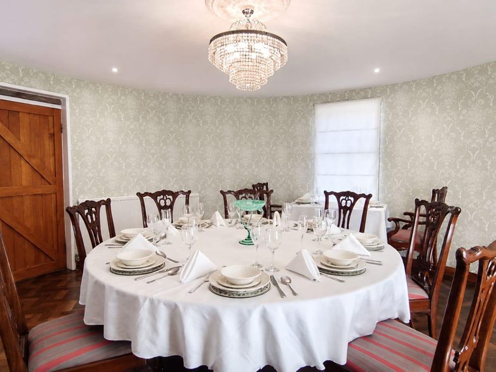 A dining room with a round table set with plates and glasses at Sharvels Oast House - Pool, Tennis, Luxury Home Peasmarsh