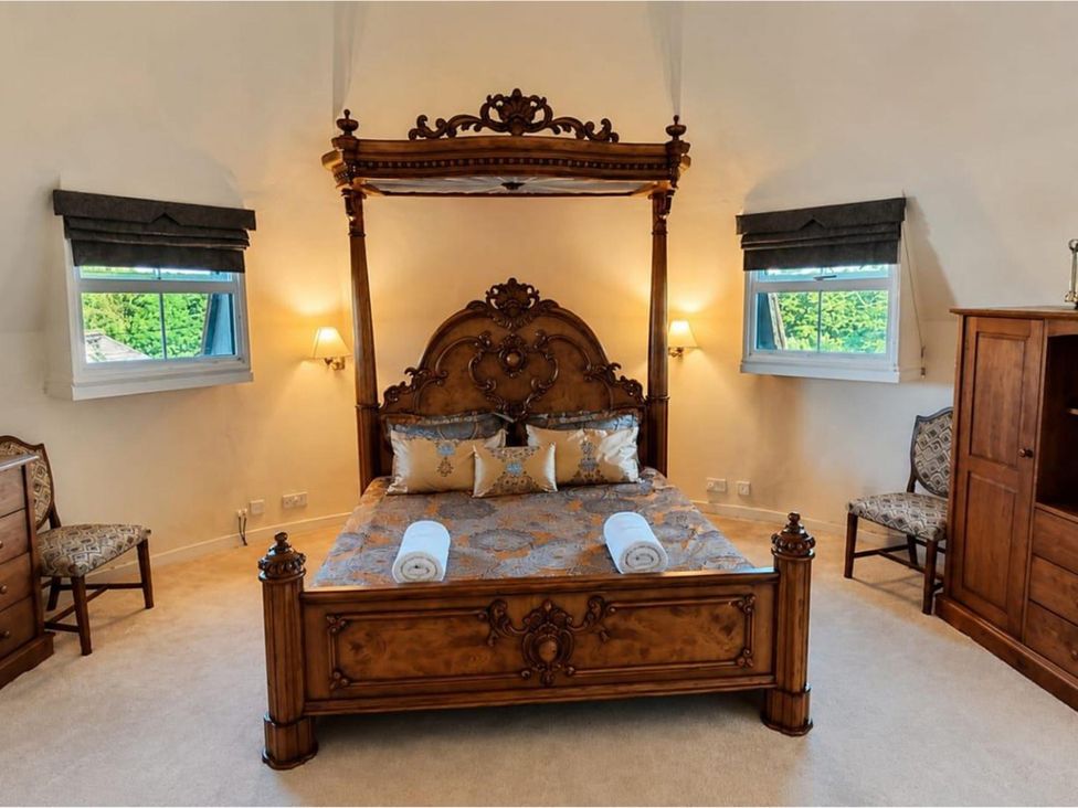 A bedroom with a wooden bed and chairs at Sharvels Oast House - Pool, Tennis, Luxury Home Peasmarsh