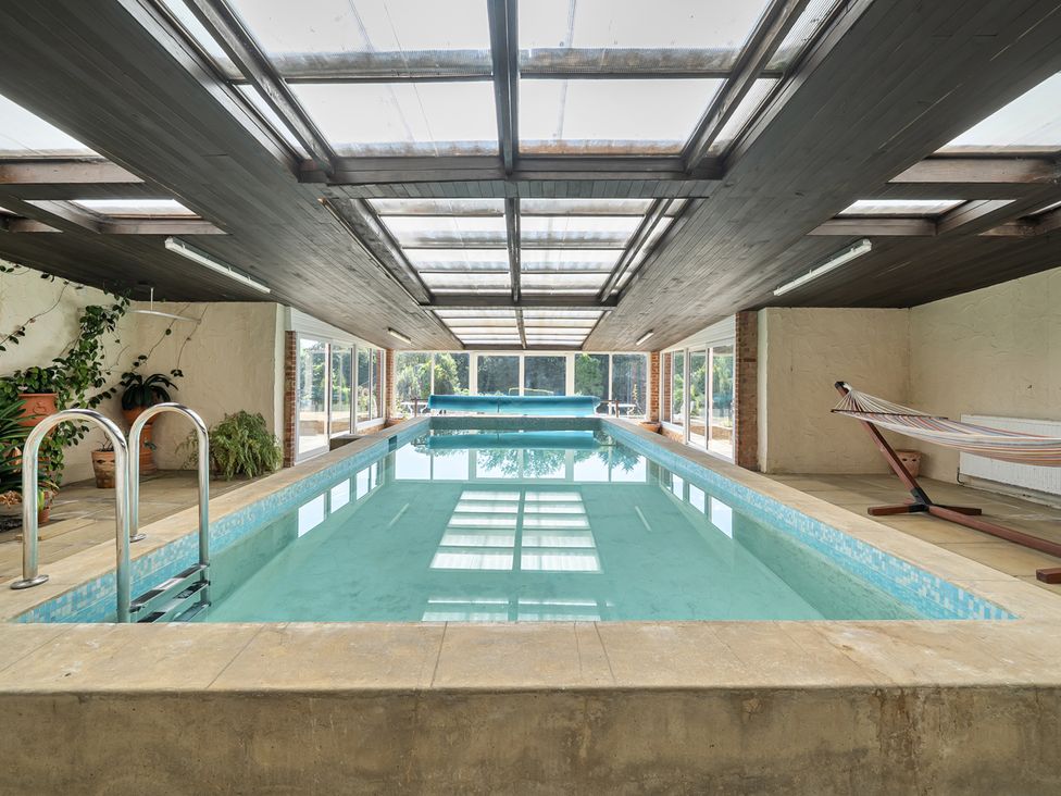 An indoor pool area with a swimming pool and hammock at Sharvels Oast House - Pool, Tennis, Luxury Home, Peasmarsh