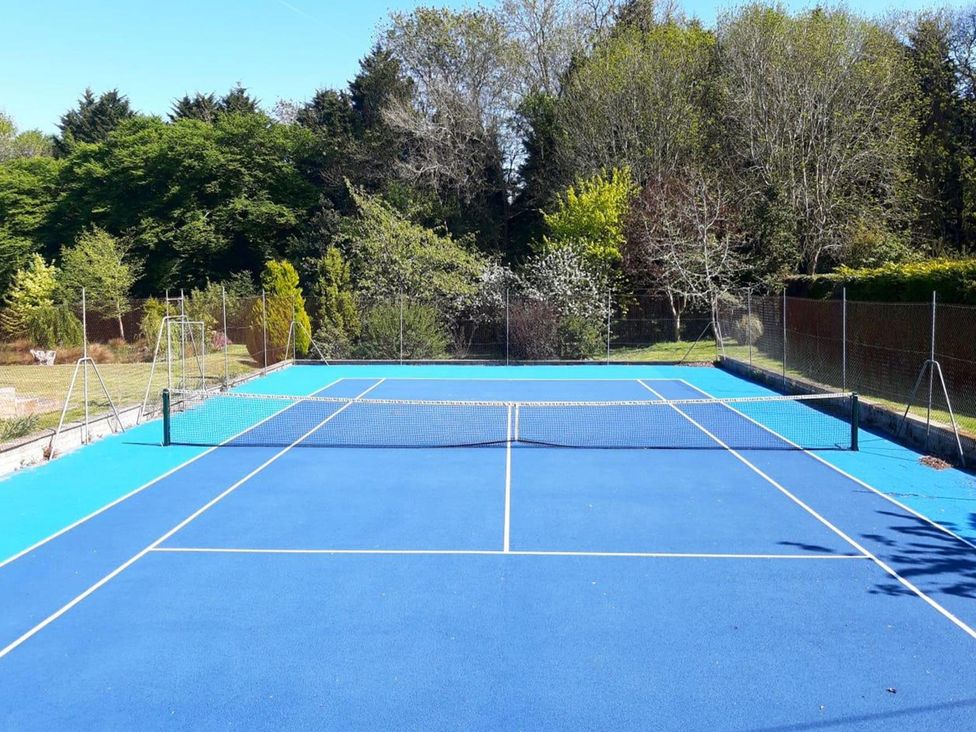 A tennis court with a net and trees at Sharvels Oast House - Pool, Tennis, Luxury Home Peasmarsh