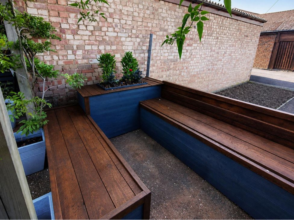 A garden with wooden benches and planters at Sharvels Oast House - Pool, Tennis, Luxury Home, Peasmarsh