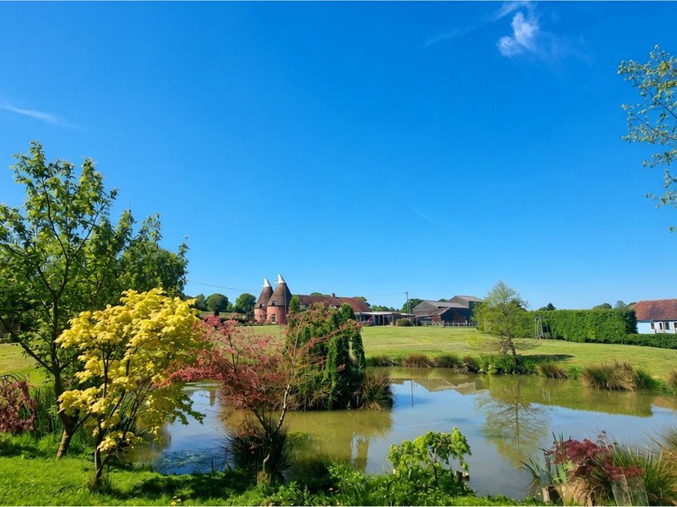 A outdoor scene featuring a pond and trees at Sharvels Oast House - Pool, Tennis, Luxury Home Peasmarsh