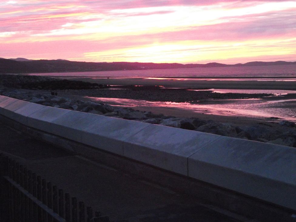 A sunset over water with rocks at Seafront Caravan - Golden Sands - 6 Berth by Your Away Stays Kinmel Bay