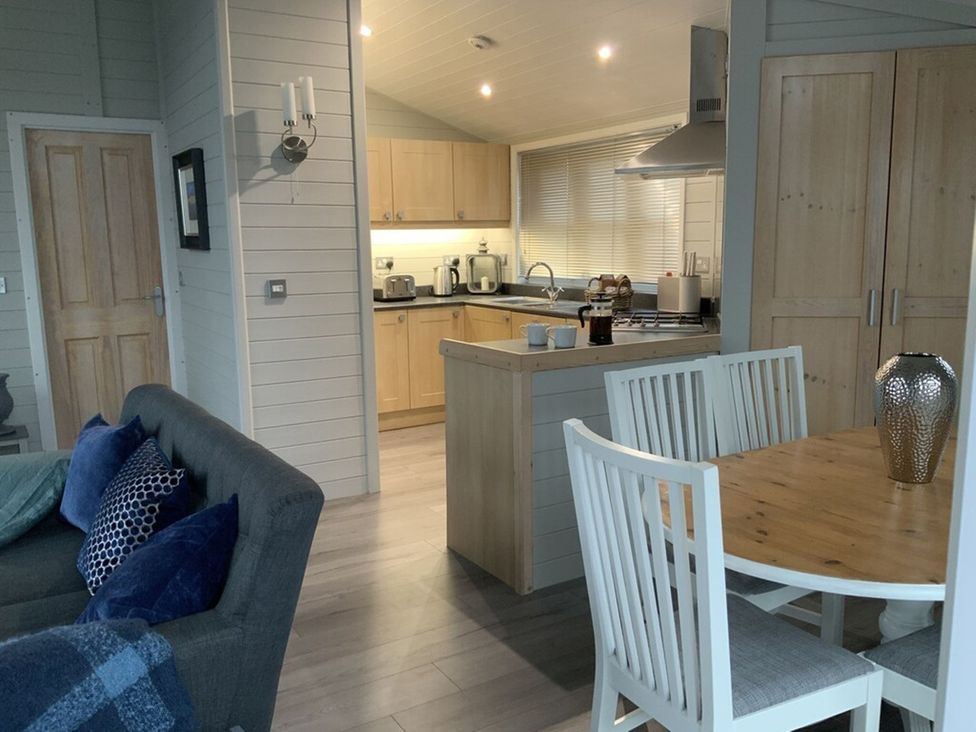 A living room with a sofa and dining area at Holly Blue - Cosy wooden lodge, Kippford