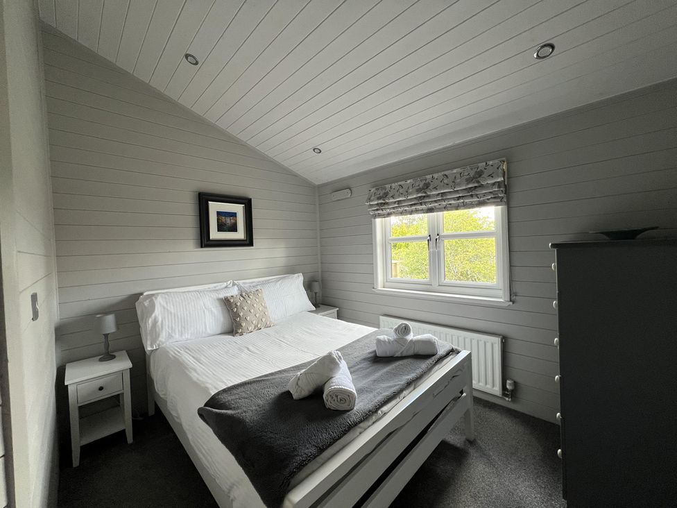 A bedroom with a bed and nightstand at Holly Blue - Cosy wooden lodge, Kippford